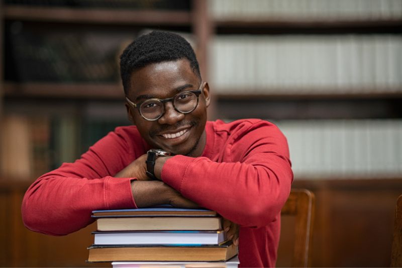 Black male student resting on a stack of books